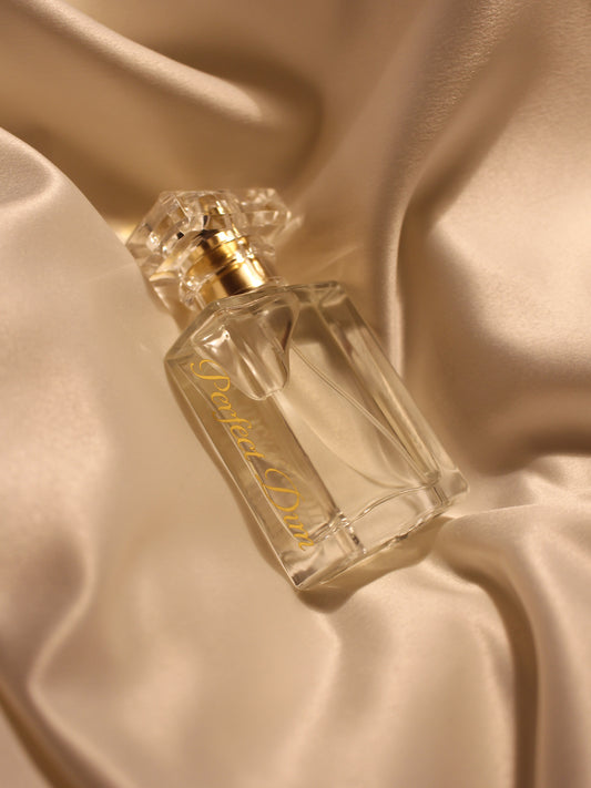 a laying bottle of perfect dim Eau de Parfum on a golden satin fabric with a crystal like cap.