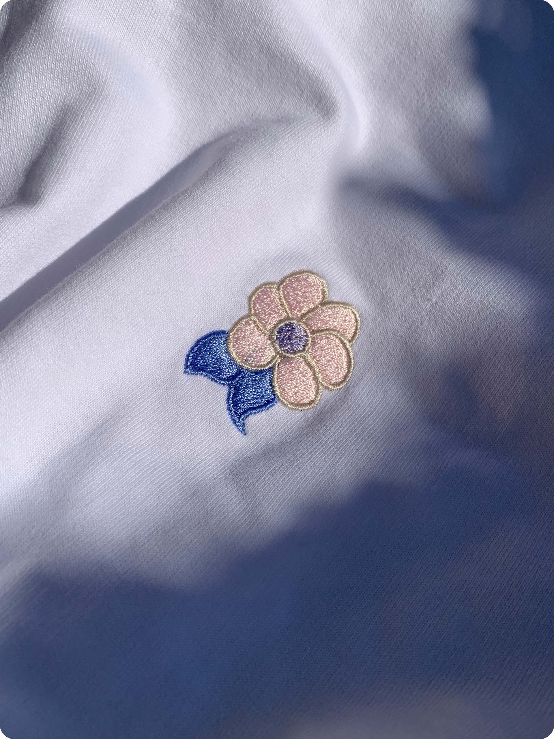 The Golden Twenties Shirts center embroidery is a stitched flower in the colors blue, lilac, gold and pink/rosé