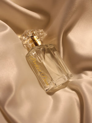 a laying bottle of perfect dim Eau de Parfum on a golden satin fabric with a crystal like cap. 