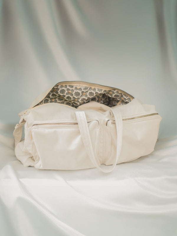 A white velvet tennis bag with golden details, placed on a cream white satin surface with a special flower pattern lining.
